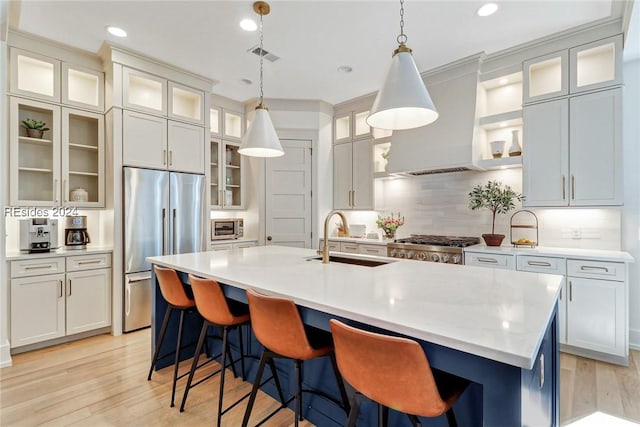 kitchen with built in fridge, sink, decorative backsplash, island exhaust hood, and a kitchen island with sink