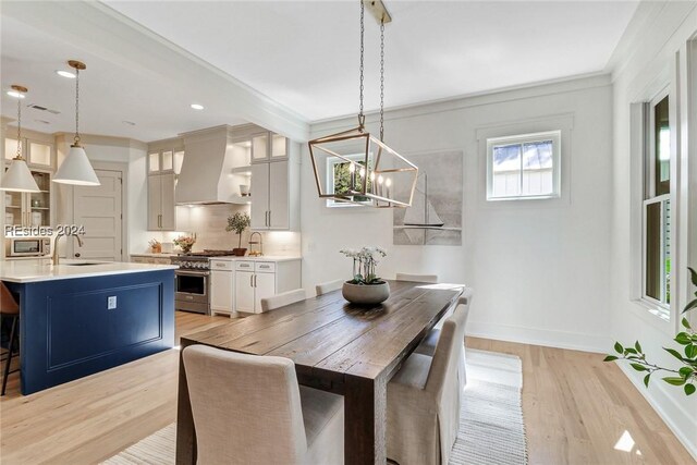 dining room with ornamental molding, sink, a chandelier, and light wood-type flooring