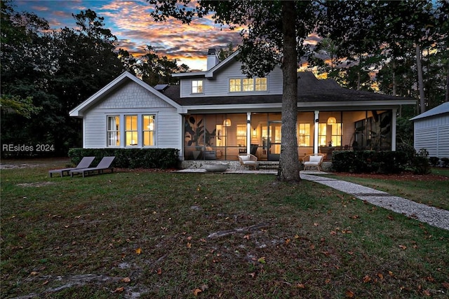 back house at dusk with a yard and a sunroom