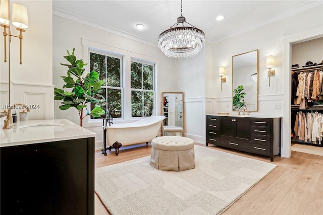 bathroom with a bathing tub, wood-type flooring, vanity, crown molding, and an inviting chandelier