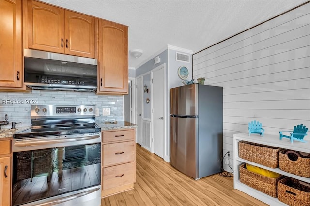 kitchen with appliances with stainless steel finishes, backsplash, light stone counters, a textured ceiling, and light wood-type flooring