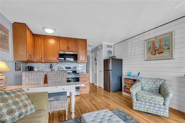 kitchen with tasteful backsplash, ornamental molding, appliances with stainless steel finishes, and light wood-type flooring