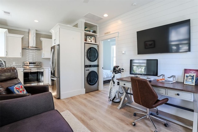 office area with built in shelves, stacked washer / dryer, wooden walls, and light wood-type flooring