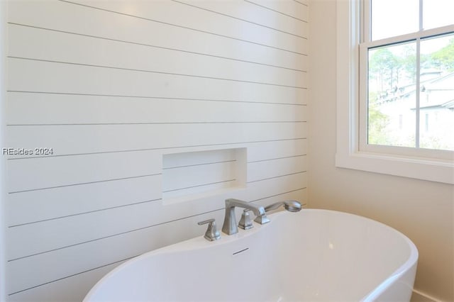 bathroom with plenty of natural light, a washtub, and wood walls