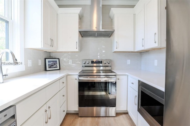 kitchen with stainless steel appliances, white cabinetry, tasteful backsplash, and wall chimney range hood