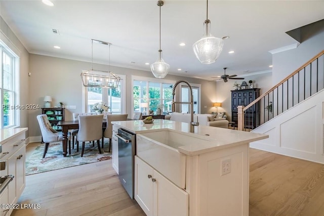 kitchen featuring sink, crown molding, hanging light fixtures, light hardwood / wood-style flooring, and an island with sink