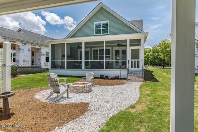 back of house featuring ceiling fan, a sunroom, a yard, and a fire pit