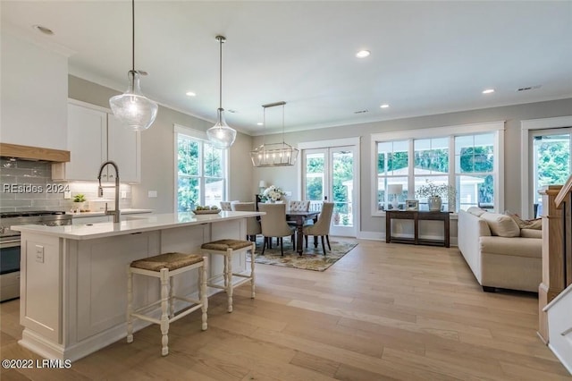 kitchen with white cabinetry, a kitchen island with sink, stainless steel range, and backsplash