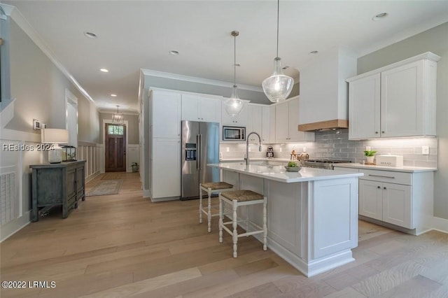 kitchen featuring pendant lighting, white cabinetry, stainless steel appliances, custom range hood, and an island with sink