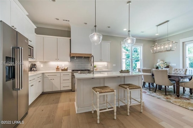 kitchen with high quality appliances, a center island with sink, white cabinets, and decorative light fixtures