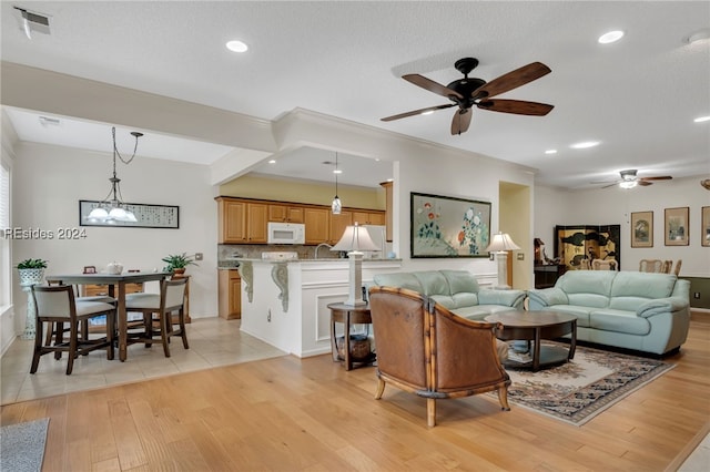 living room featuring crown molding, ceiling fan with notable chandelier, a textured ceiling, and light hardwood / wood-style floors