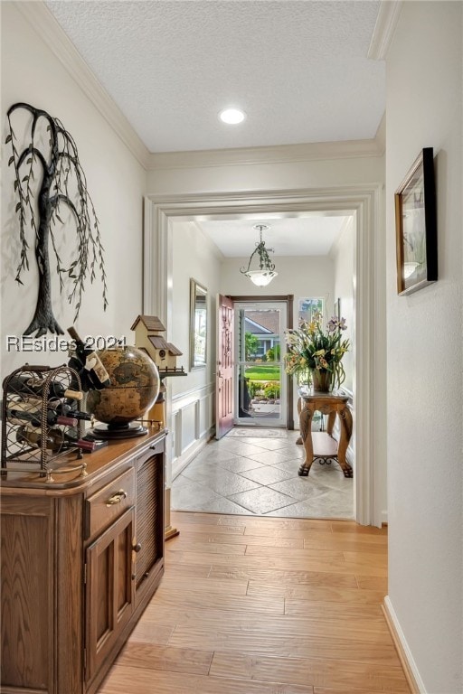 hall featuring an inviting chandelier, ornamental molding, light hardwood / wood-style floors, and a textured ceiling