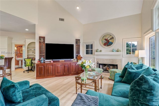 living room with a high end fireplace, high vaulted ceiling, and light wood-type flooring