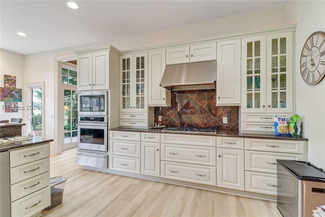 kitchen with appliances with stainless steel finishes, backsplash, white cabinets, dark stone counters, and light wood-type flooring