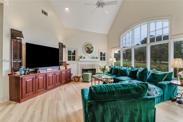 living room with ceiling fan, light hardwood / wood-style floors, high vaulted ceiling, and a tile fireplace