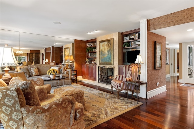 living room with a large fireplace, a chandelier, built in features, and dark hardwood / wood-style floors