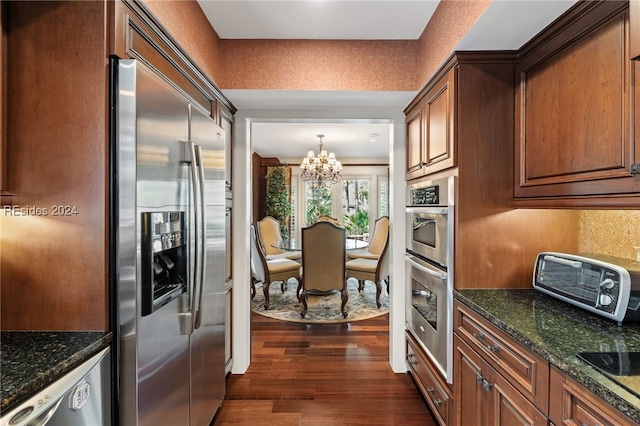 kitchen with dark wood-type flooring, stainless steel appliances, a chandelier, and dark stone countertops