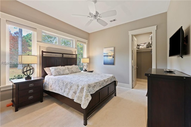 bedroom with ceiling fan, a spacious closet, light colored carpet, and a closet