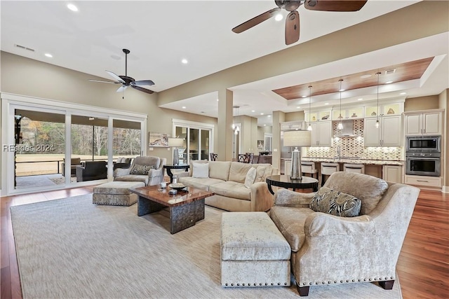 living room featuring a raised ceiling, ceiling fan, and light hardwood / wood-style floors