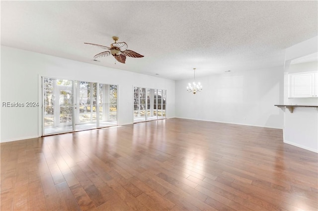 unfurnished living room featuring dark wood-type flooring, ceiling fan with notable chandelier, and a textured ceiling