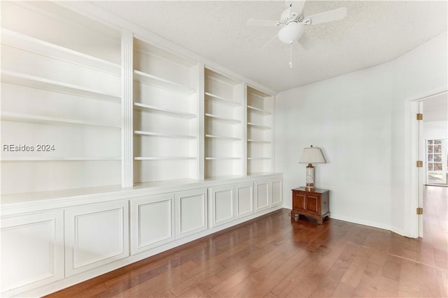 unfurnished living room with ceiling fan, dark wood-type flooring, built in features, and a textured ceiling