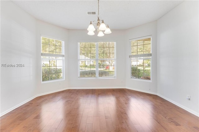 unfurnished dining area featuring wood-type flooring, a chandelier, and a healthy amount of sunlight