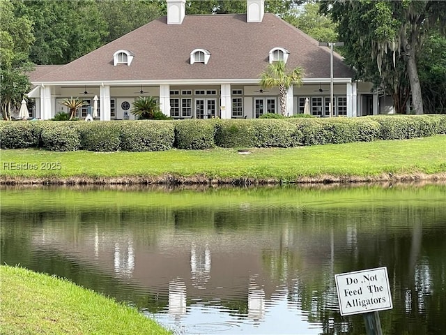 back of property with a water view, ceiling fan, and a lawn