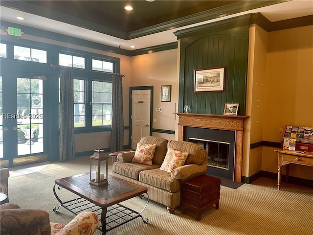 living room featuring a tray ceiling, carpet floors, ornamental molding, and a large fireplace