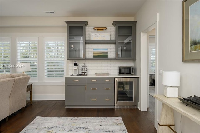 bar featuring wine cooler, backsplash, dark wood-type flooring, and gray cabinets