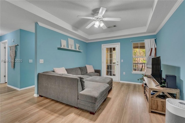 living room with ceiling fan, a tray ceiling, and light wood-type flooring