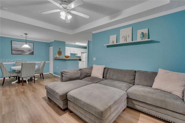 living room featuring a raised ceiling, ceiling fan, ornamental molding, and light hardwood / wood-style floors