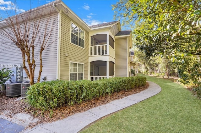 view of home's exterior with central AC, a balcony, a sunroom, and a lawn