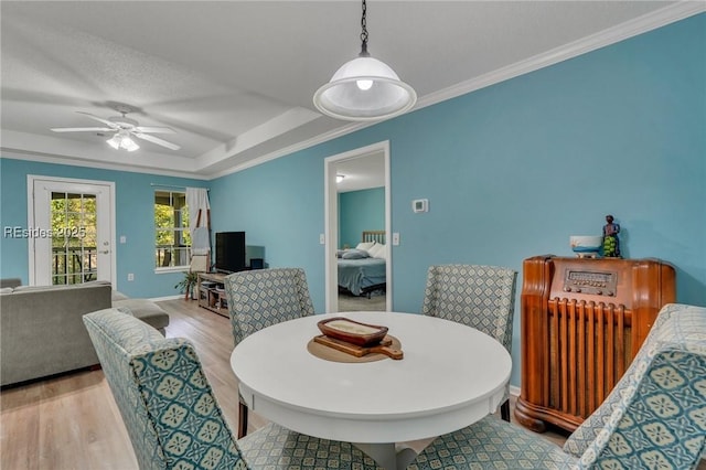 dining space with crown molding, a tray ceiling, a textured ceiling, and light wood-type flooring