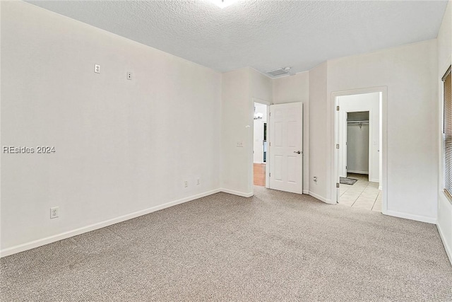 unfurnished bedroom featuring a walk in closet, light colored carpet, a textured ceiling, and a closet