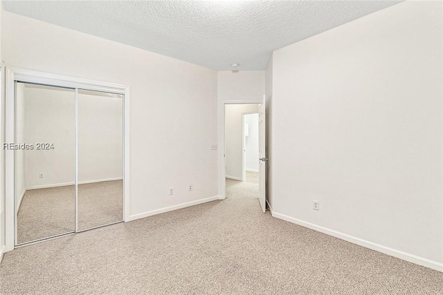 unfurnished bedroom featuring light carpet, a closet, and a textured ceiling