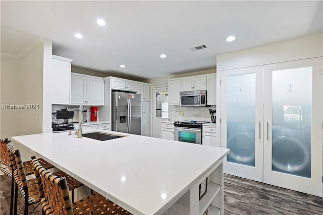 kitchen with a kitchen bar, sink, appliances with stainless steel finishes, white cabinets, and backsplash