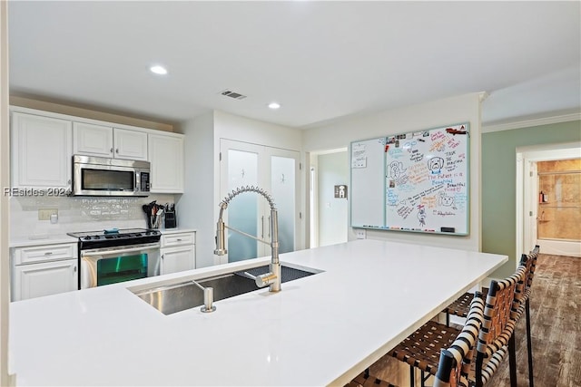 kitchen with sink, a breakfast bar area, white cabinets, backsplash, and stainless steel appliances