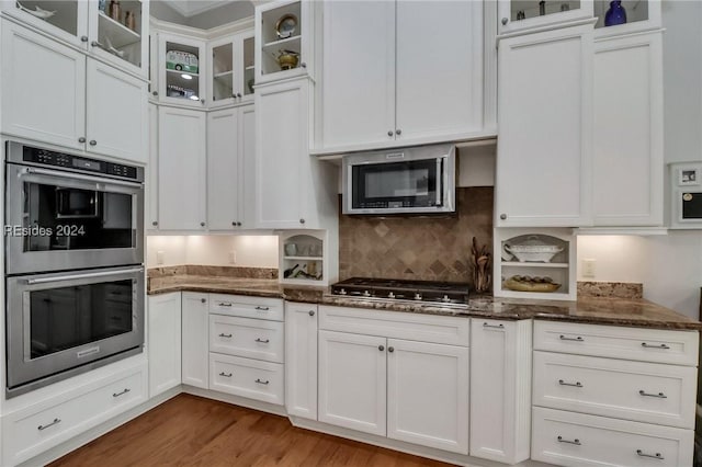 kitchen featuring white cabinetry, stainless steel appliances, dark stone counters, and light wood-type flooring