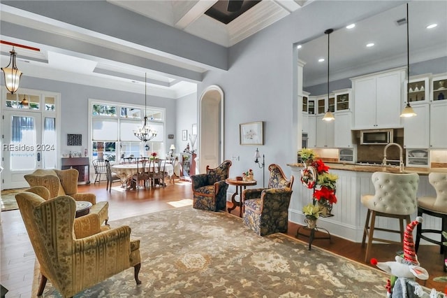 living room with beamed ceiling, a chandelier, dark hardwood / wood-style flooring, coffered ceiling, and crown molding