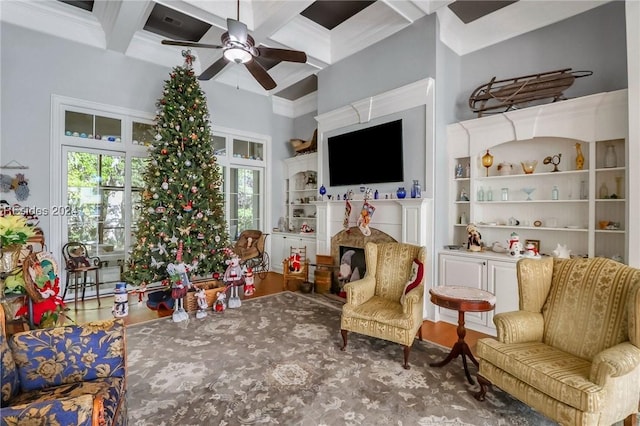 living area with beamed ceiling, a fireplace, coffered ceiling, and ceiling fan