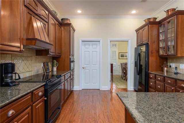 kitchen featuring backsplash, hardwood / wood-style floors, custom exhaust hood, and black appliances