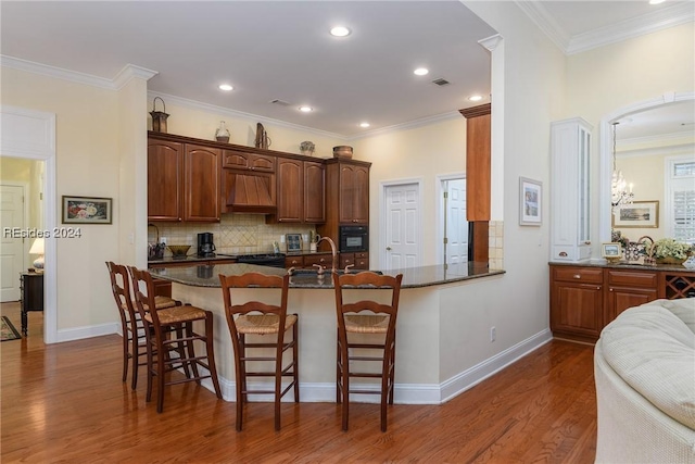 kitchen featuring a breakfast bar, premium range hood, kitchen peninsula, dark hardwood / wood-style flooring, and dark stone counters