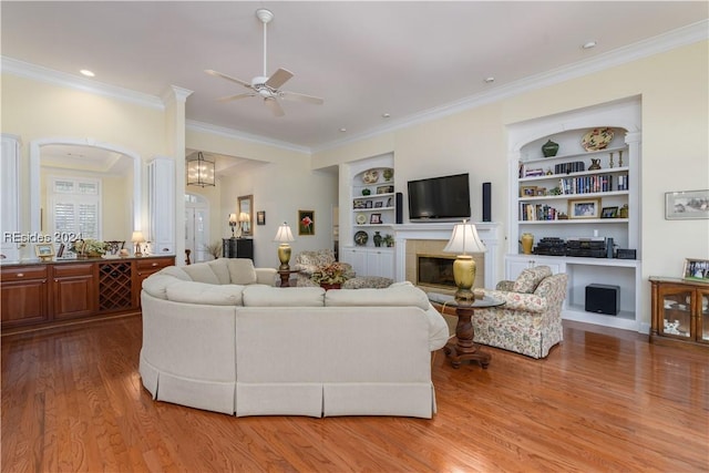 living room with crown molding, built in shelves, light hardwood / wood-style flooring, and ceiling fan