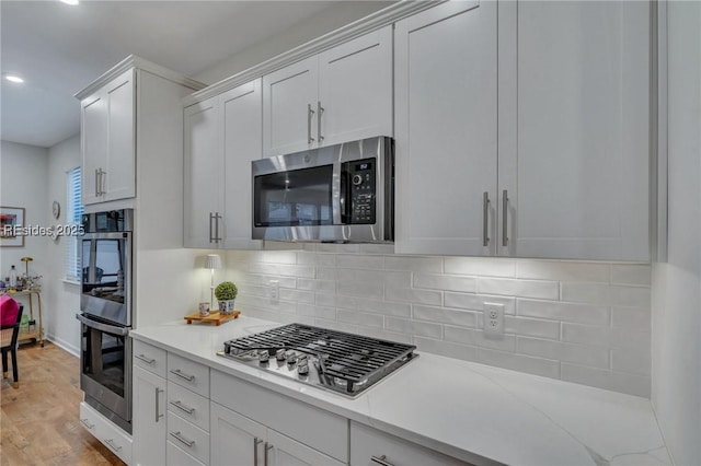 kitchen featuring white cabinetry, light wood-type flooring, appliances with stainless steel finishes, light stone countertops, and decorative backsplash