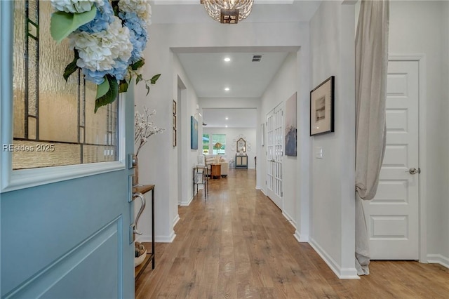 hall with light hardwood / wood-style floors and a notable chandelier