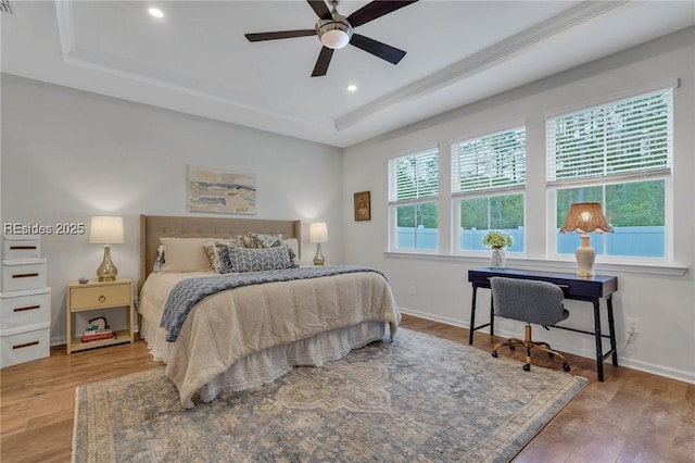 bedroom featuring ceiling fan, wood-type flooring, and a tray ceiling