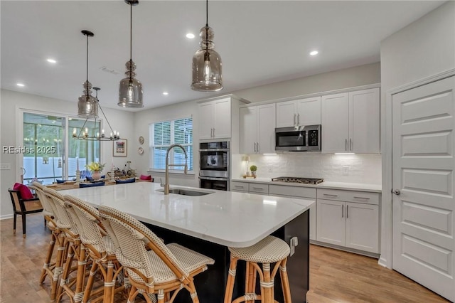 kitchen with stainless steel appliances, sink, a center island with sink, and white cabinets