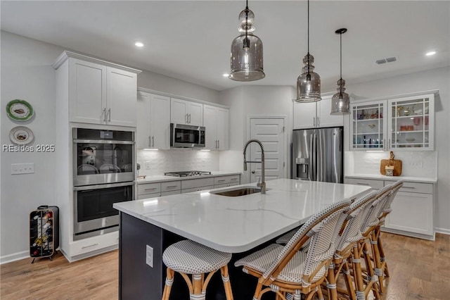 kitchen with appliances with stainless steel finishes, sink, white cabinets, backsplash, and a kitchen island with sink