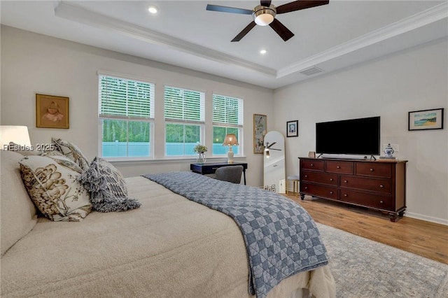 bedroom with ceiling fan, ornamental molding, a raised ceiling, and light hardwood / wood-style floors