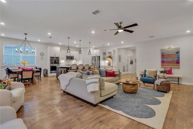 living room with ceiling fan with notable chandelier and light wood-type flooring